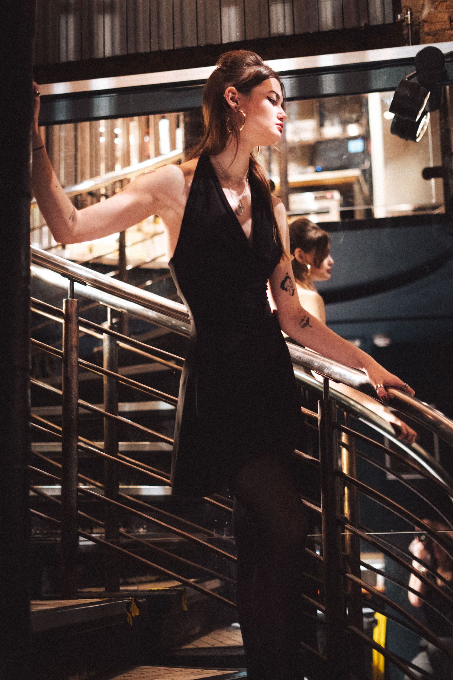An elegant figure in a black outfit poses on a staircase with metal railings.