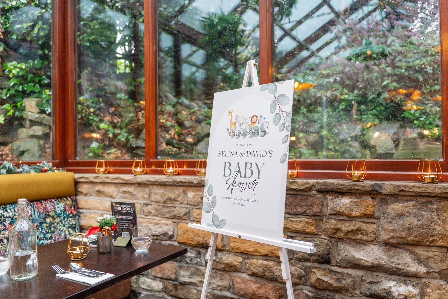 Baby shower decorations and signage displayed along stone wall in sunlit venue space.