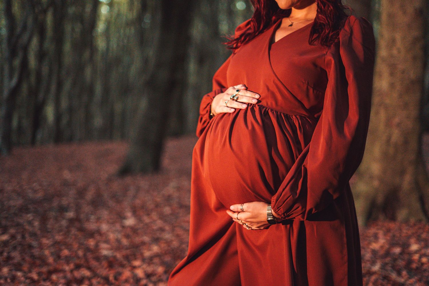 Figure in flowing red dress and hat poses dramatically against autumn forest backdrop.