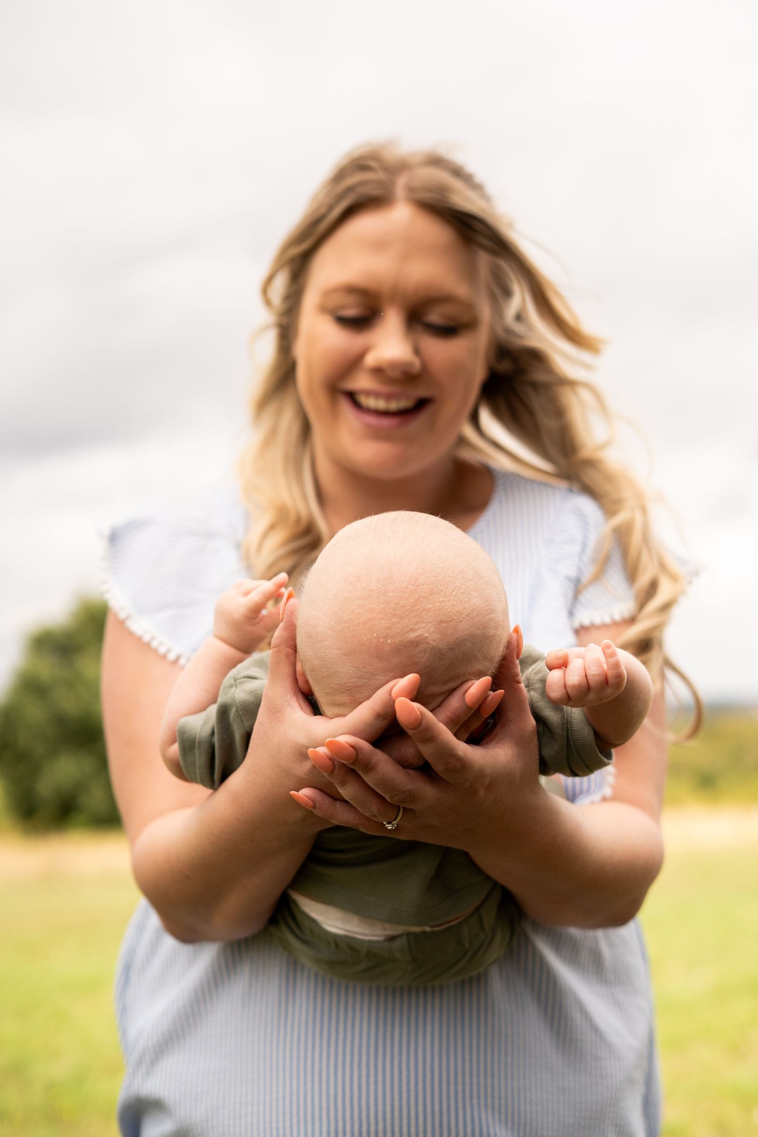 Parent lifting baby up against cloudy sky in outdoor setting.