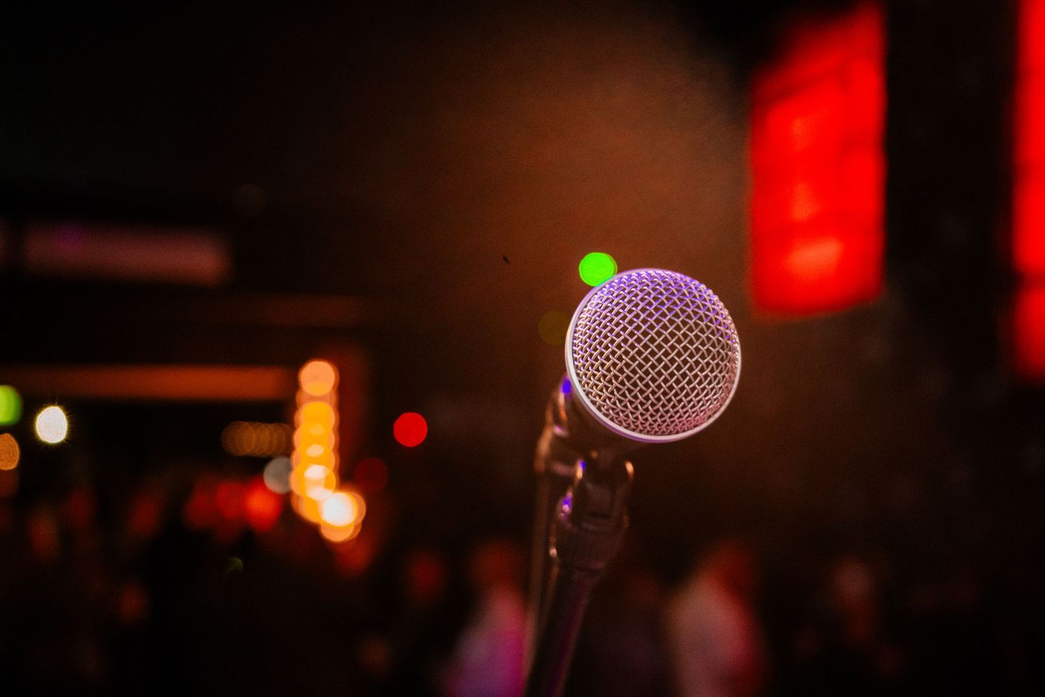 A microphone stands illuminated against a dark background with red lighting and bokeh effects.