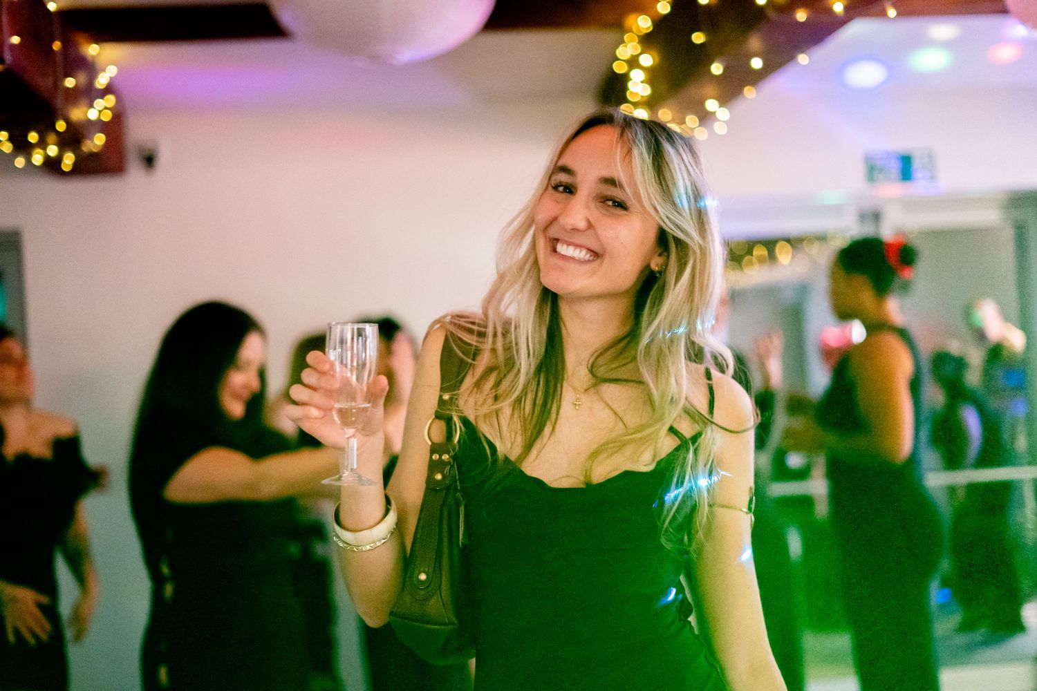 Party guests dancing under festive holiday lights in an indoor venue.