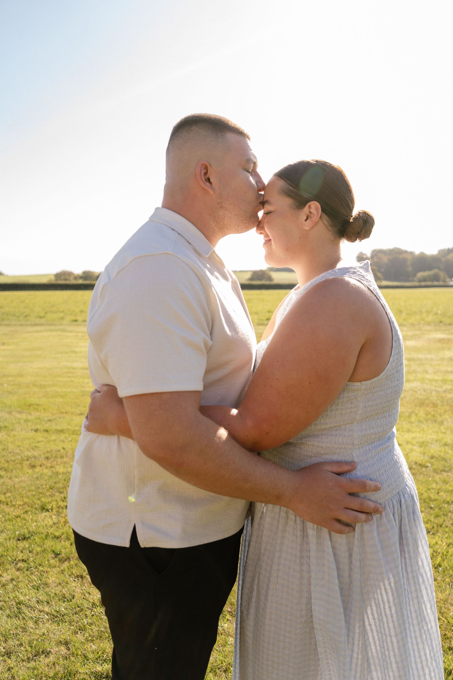 A tender moment between a couple backlit by golden sunlight in an open field.