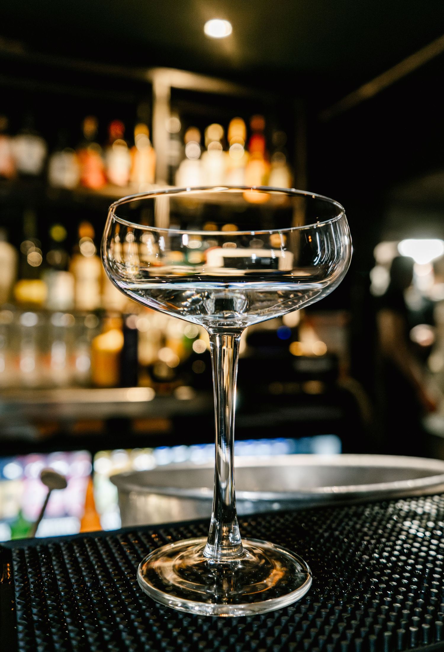 Empty coupe cocktail glasses arranged on a black rubber bar mat.