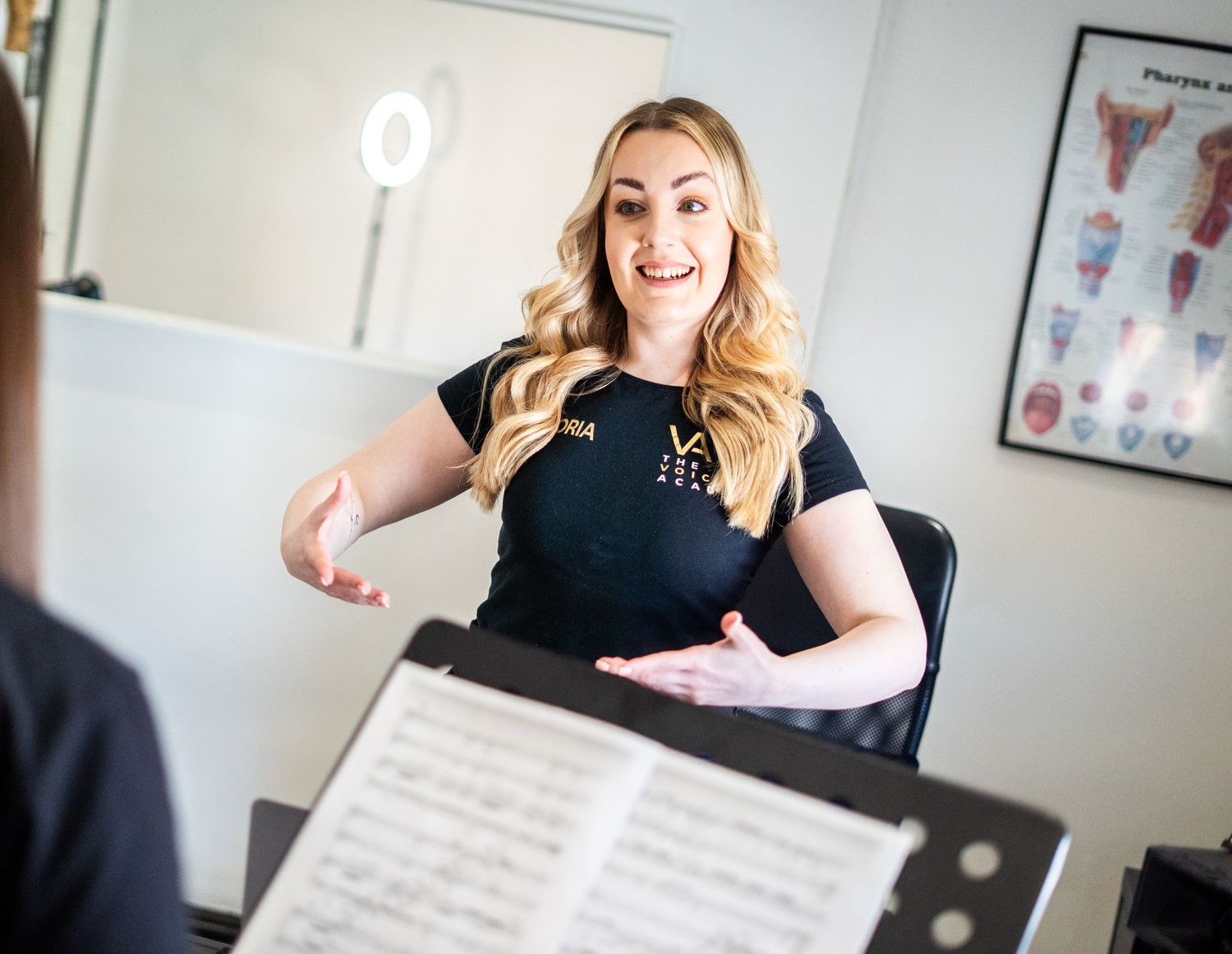 Vocal coach teaching with animated expression in front of music stand.