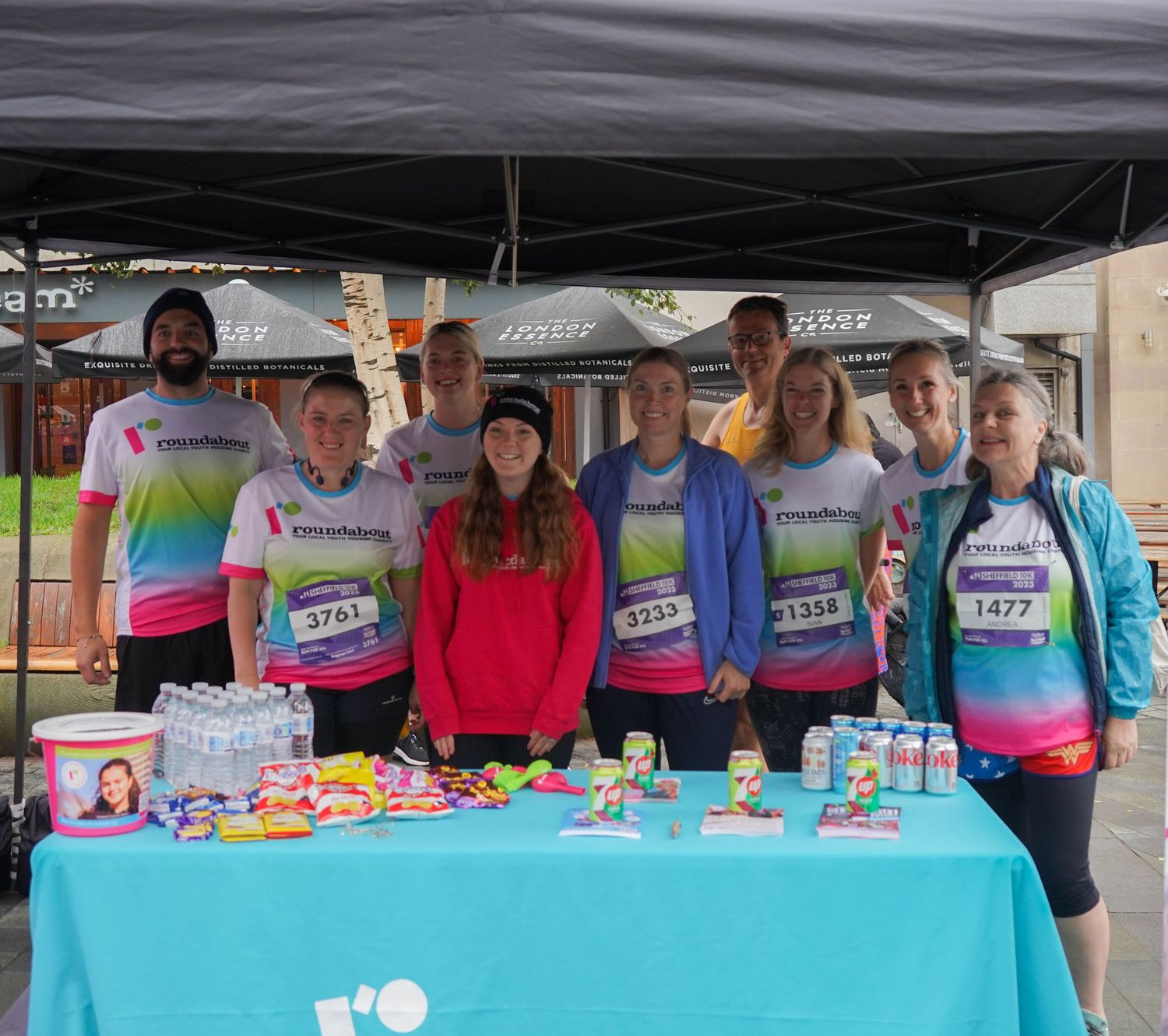 Participants gather around a refreshment table with snacks and drinks at a charity running event.