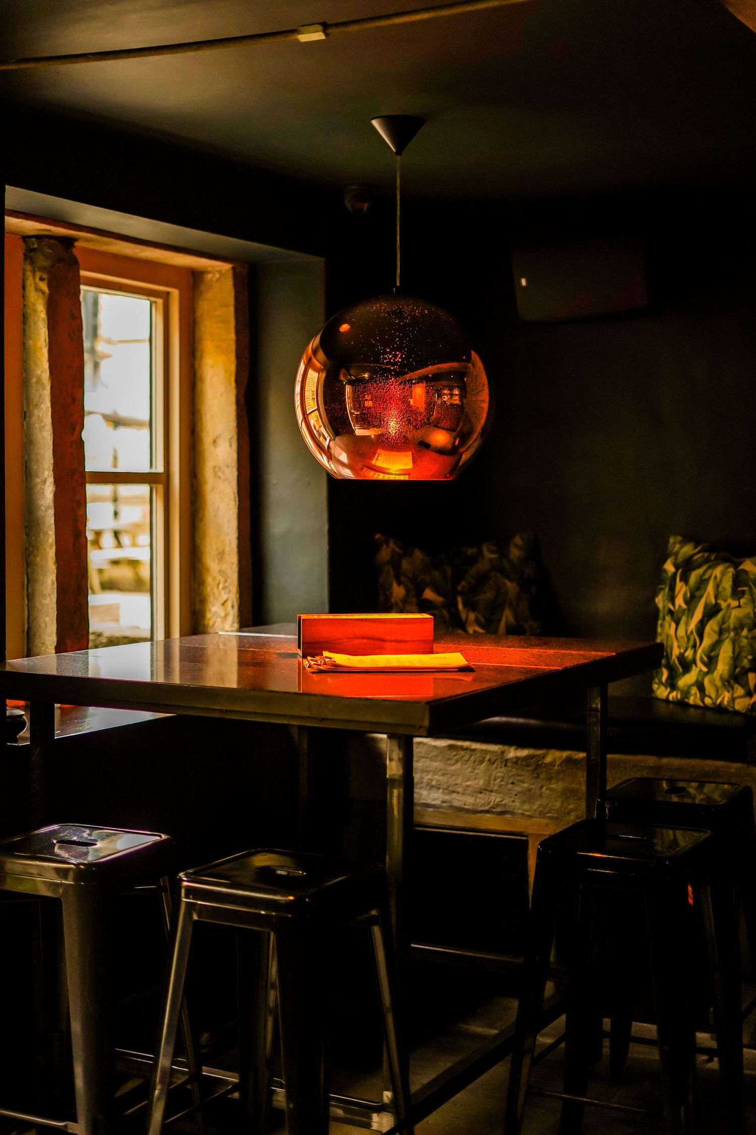 Moody restaurant interior with copper pendant lamp hanging over dark wooden table and bench seating.