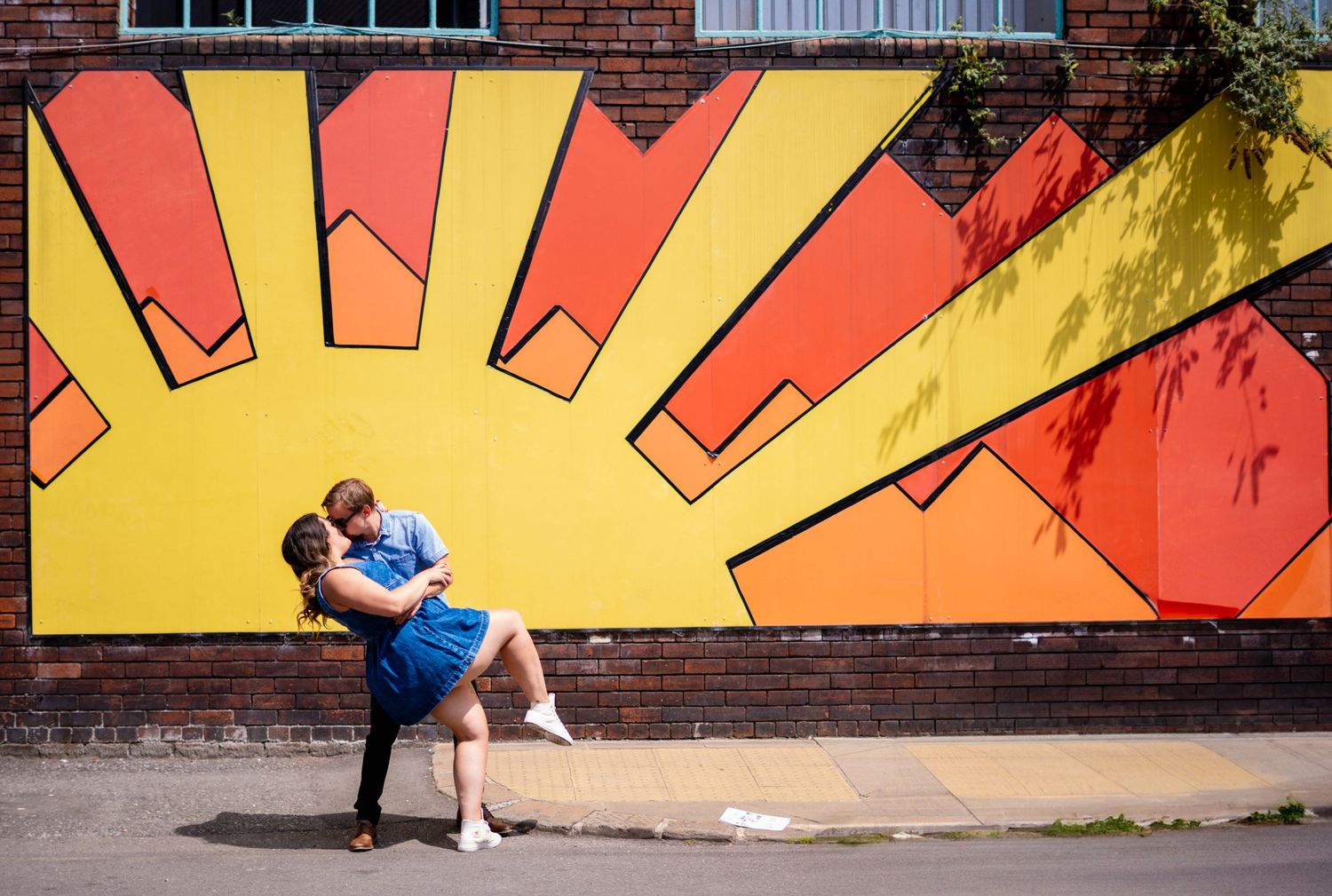 Couple posing against vibrant street art mural with geometric sunburst design.