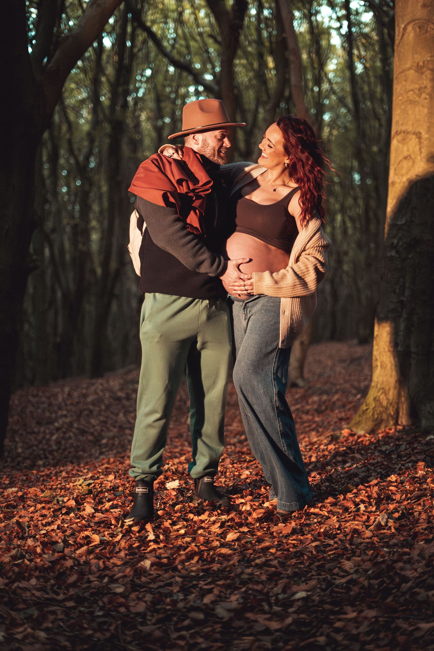Two people embracing in autumn forest surrounded by fallen leaves and tree trunks.