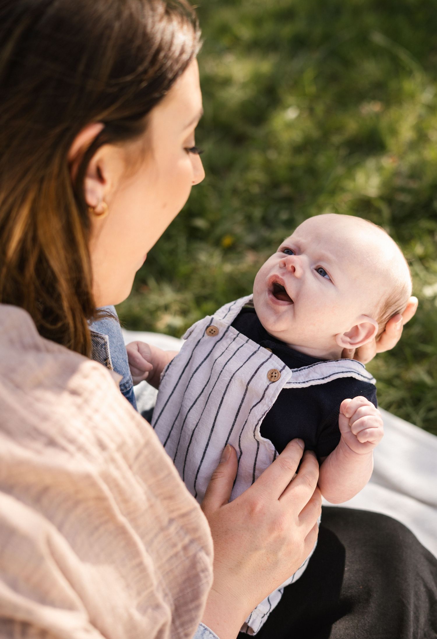 Baby in striped outfit sharing joyful moments outdoors on a sunny day.