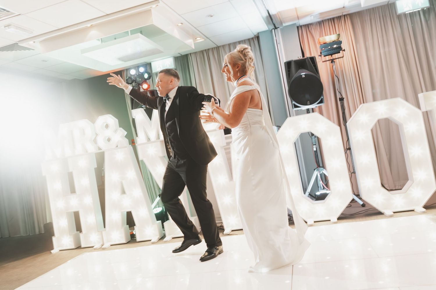 Wedding couple dancing in an elegant white reception venue with soft lighting.