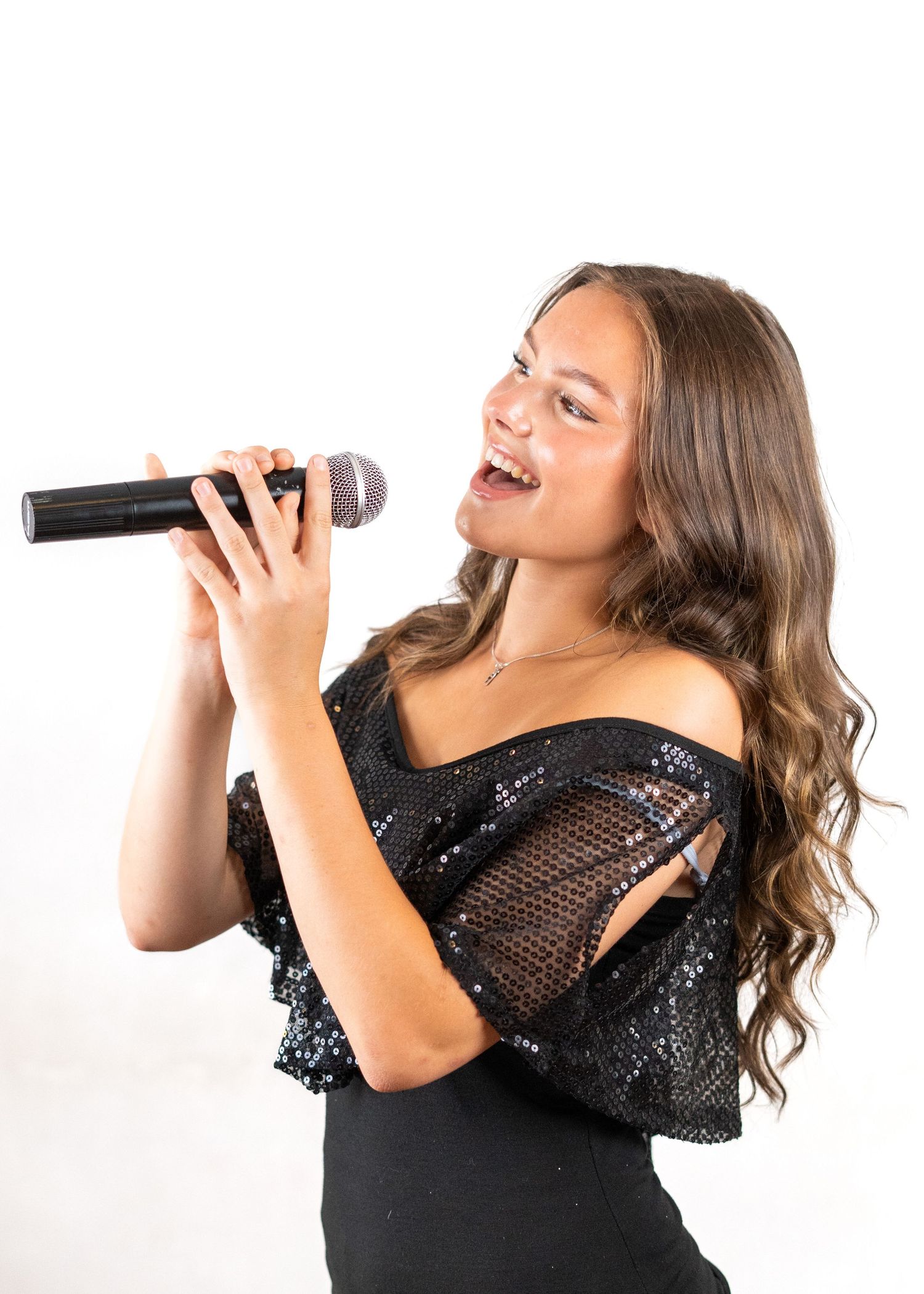 Singer in a sparkly black dress performs with a microphone against a white background.