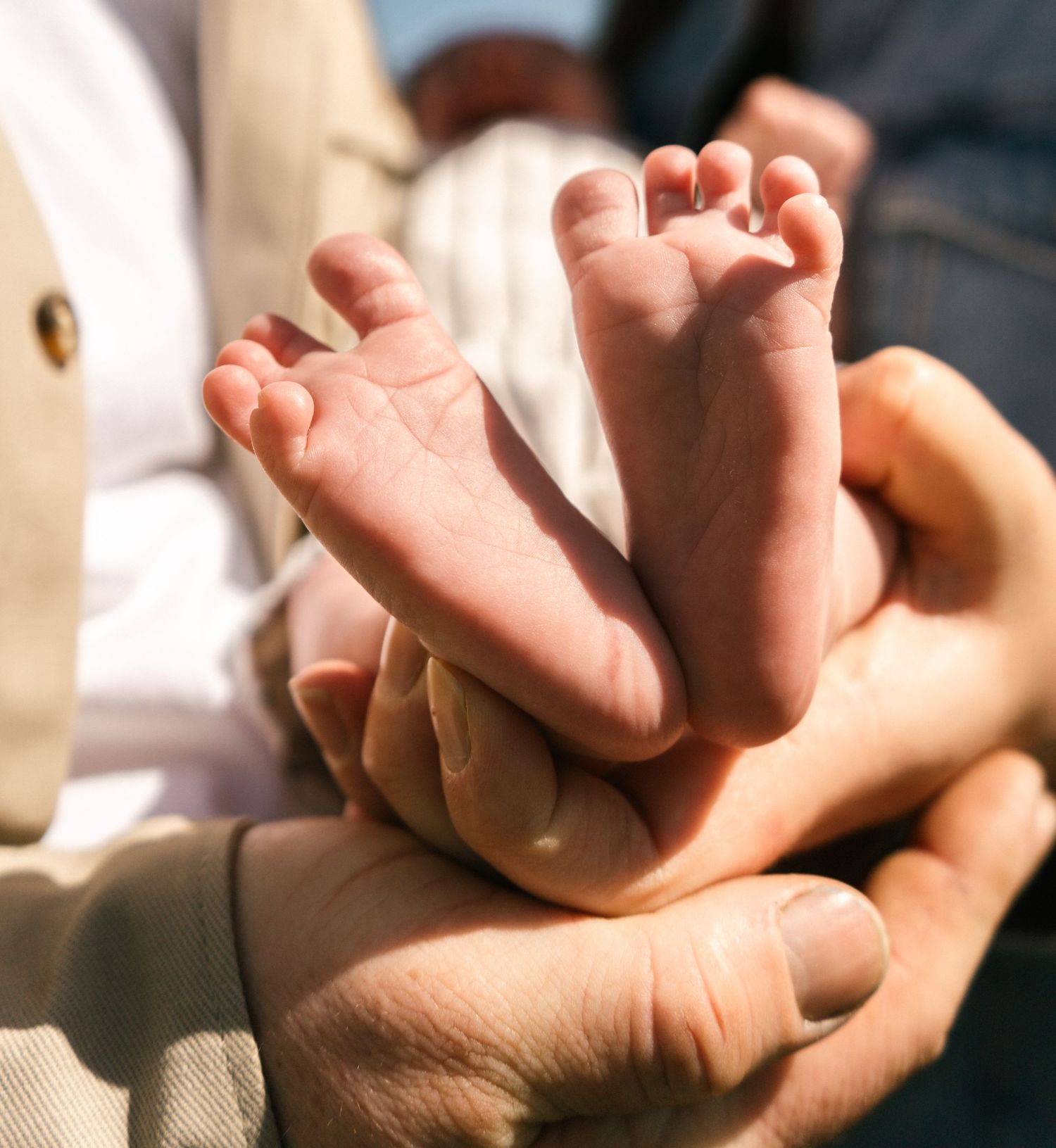Newborn baby's tiny feet resting in caring hands against a soft white background.
