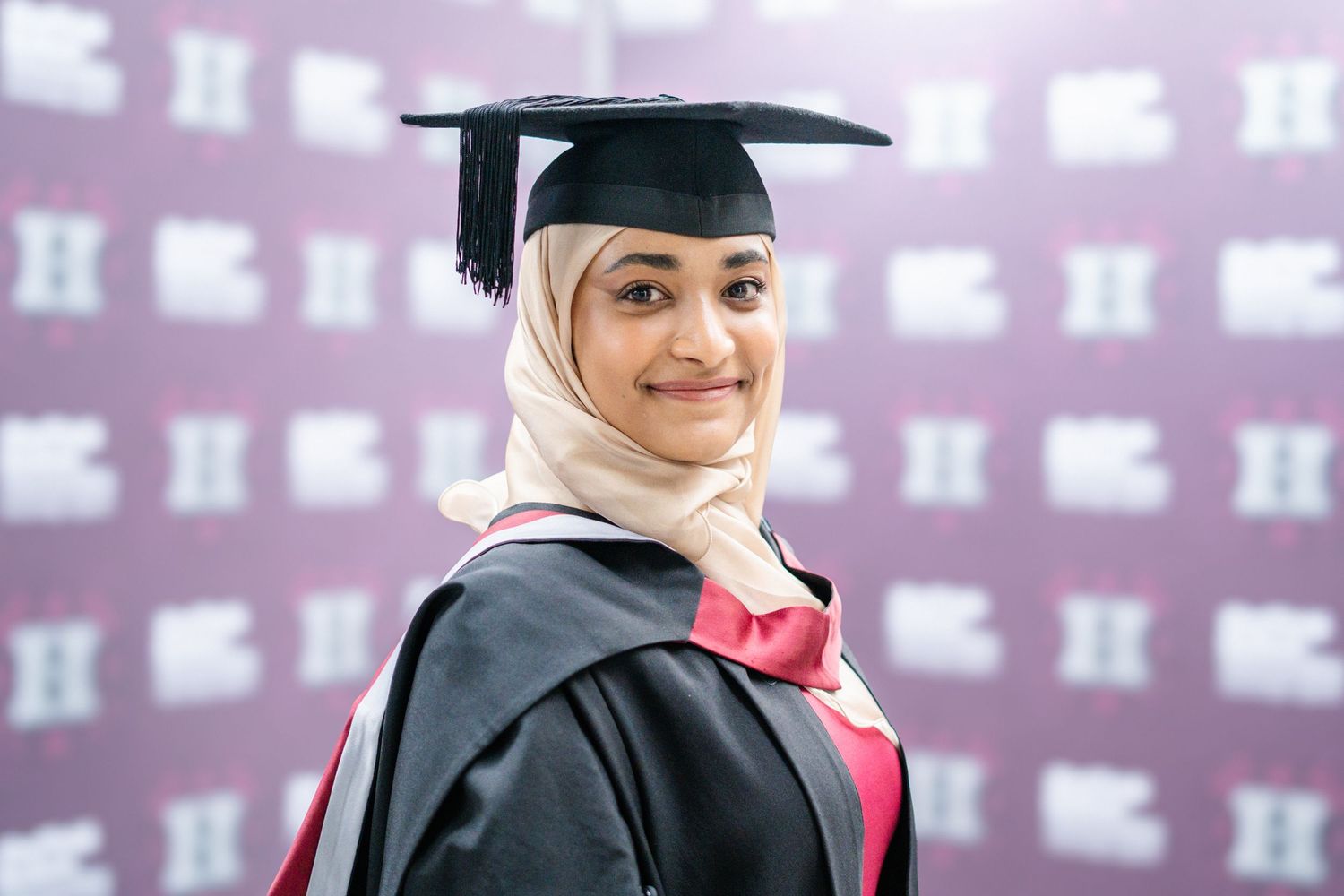 Graduate in academic regalia posing against a purple backdrop.