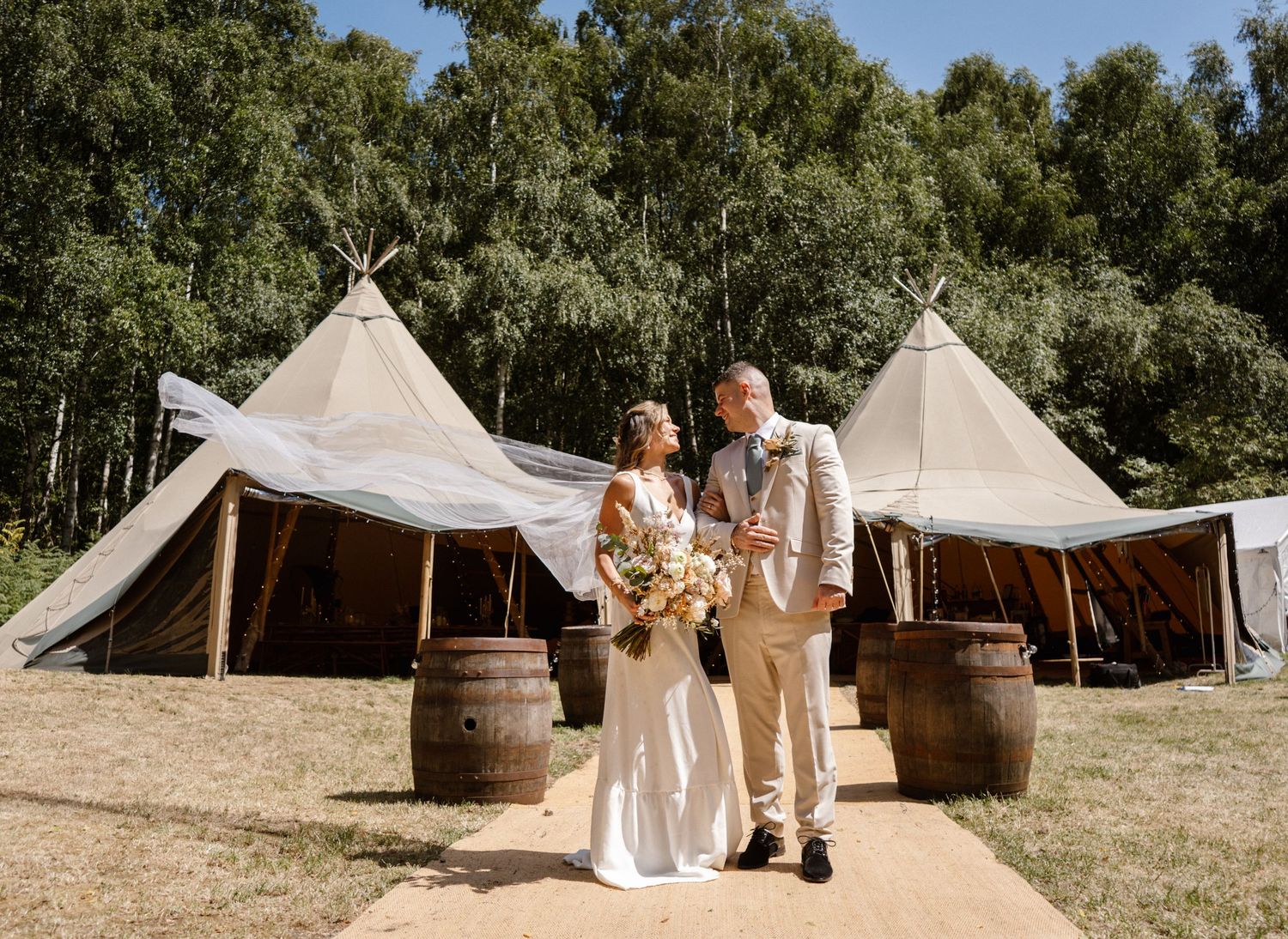 Rustic outdoor wedding venue with teepee tents and wooden barrel decorations.