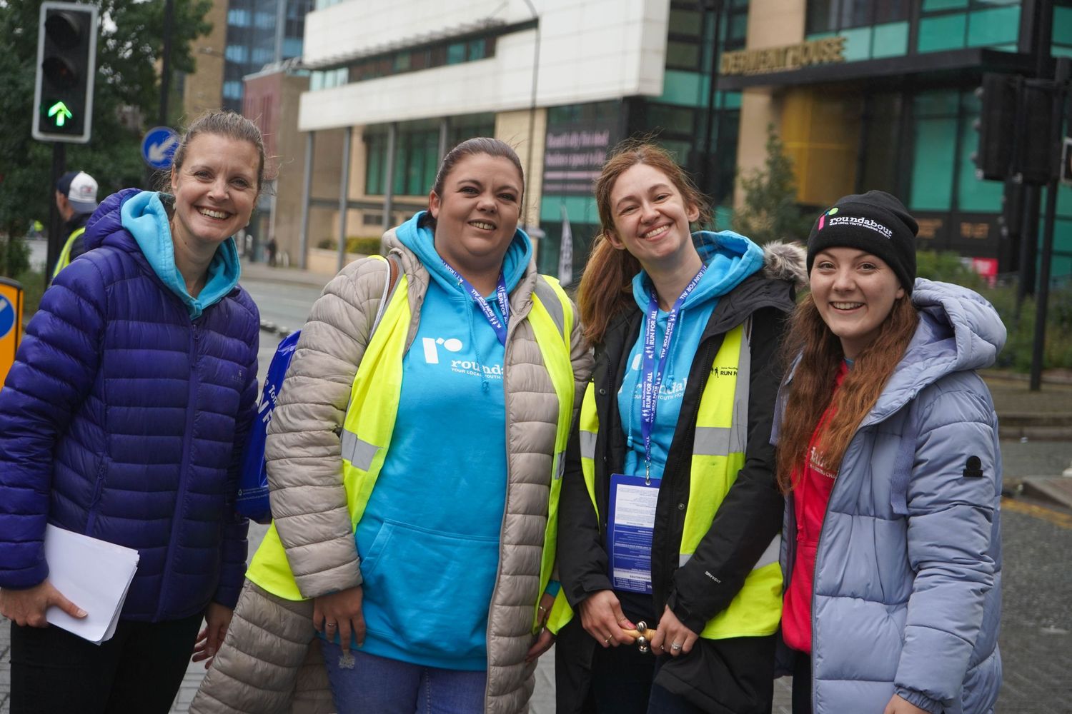 Spectators and race volunteers in high-visibility vests watching from the sidelines of a running event.