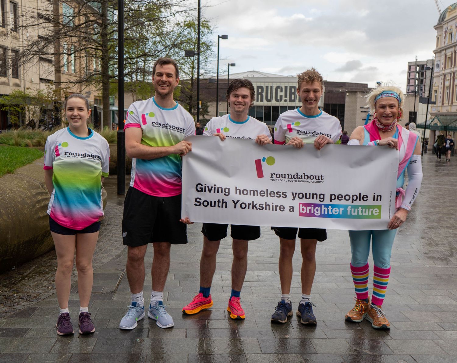 Group of runners hold Roundabout charity banner supporting homeless youth initiative.