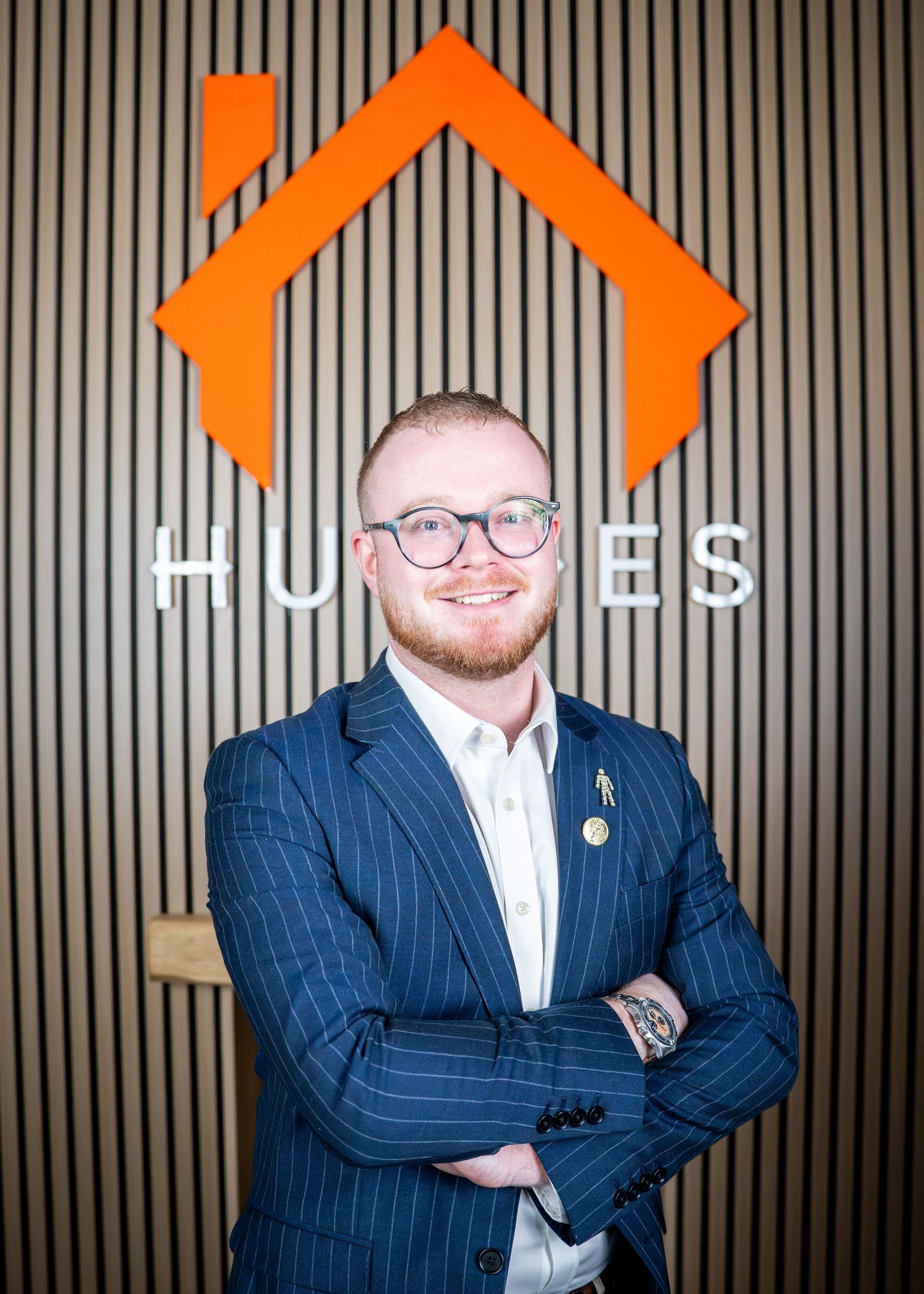 Professional in navy pinstripe suit poses against modern office backdrop.