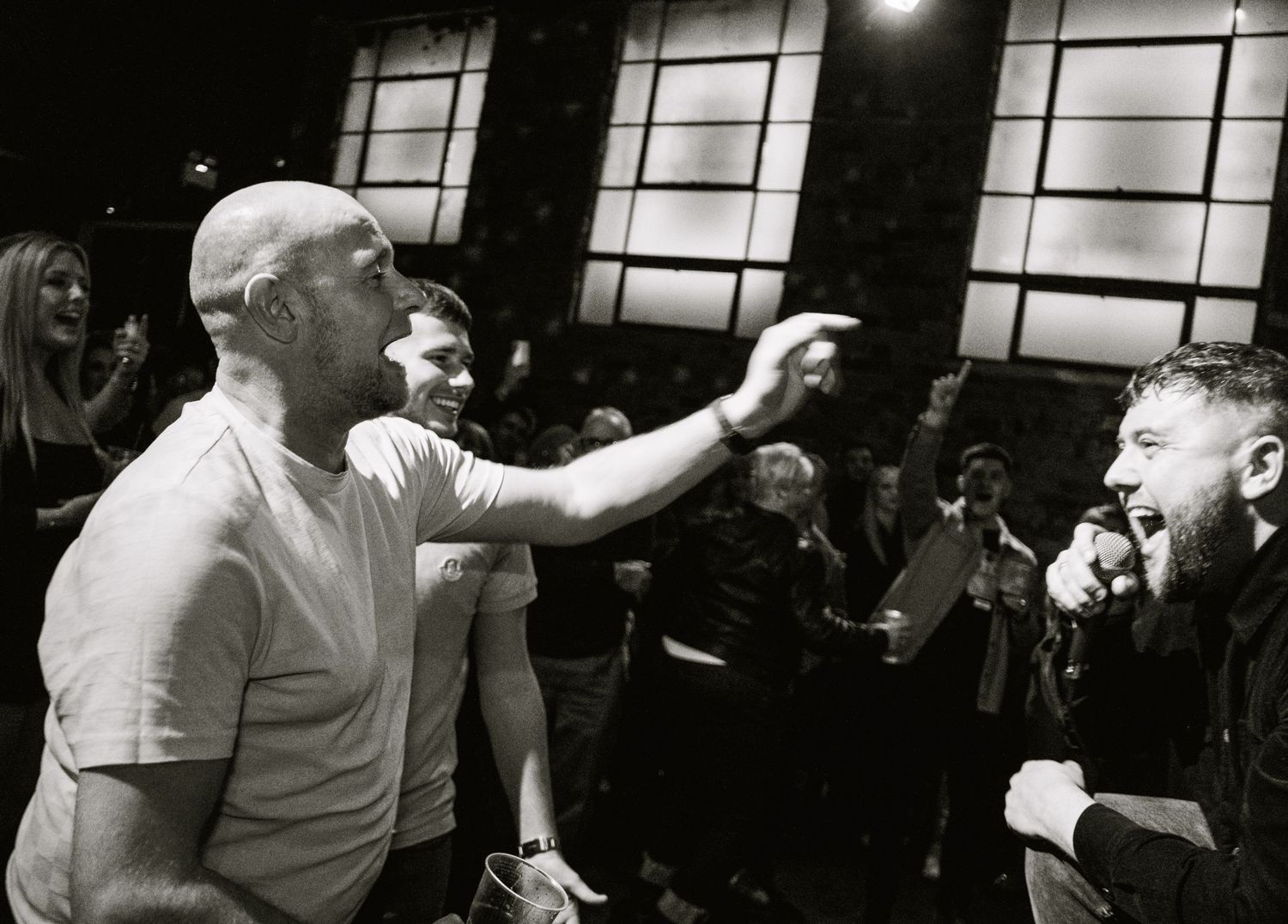 Black and white concert photo showing performers engaging with audience in intimate venue setting.