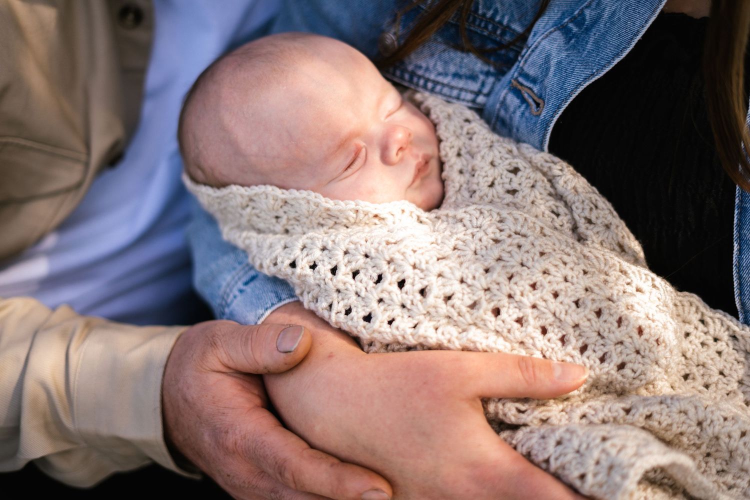 Sleeping newborn wrapped in cozy crocheted blanket held in gentle hands.