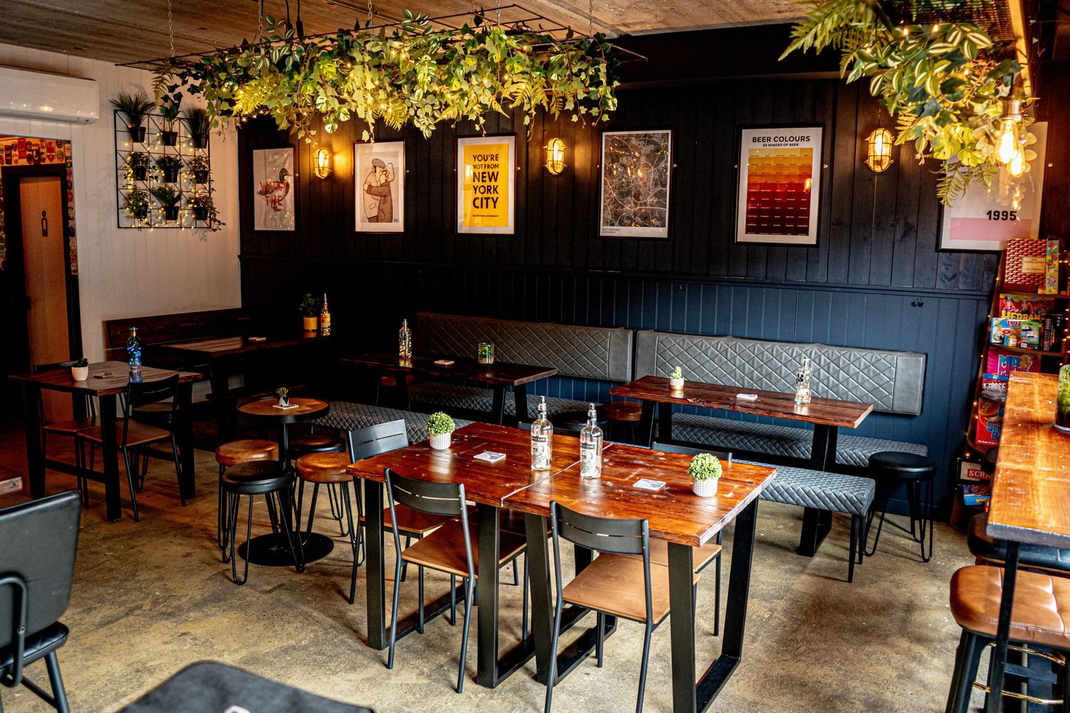 Restaurant interior with wooden tables, booth seating, and lush greenery hanging from above.