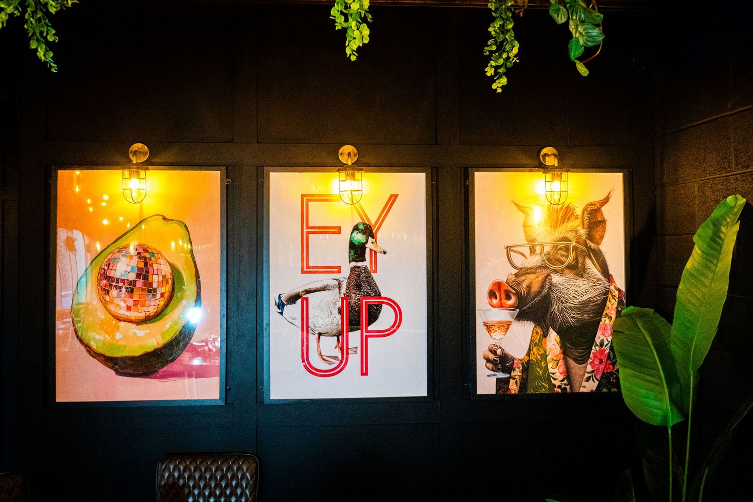 Illuminated wall art display with tropical plants and modern framed pieces in a dimly lit space.