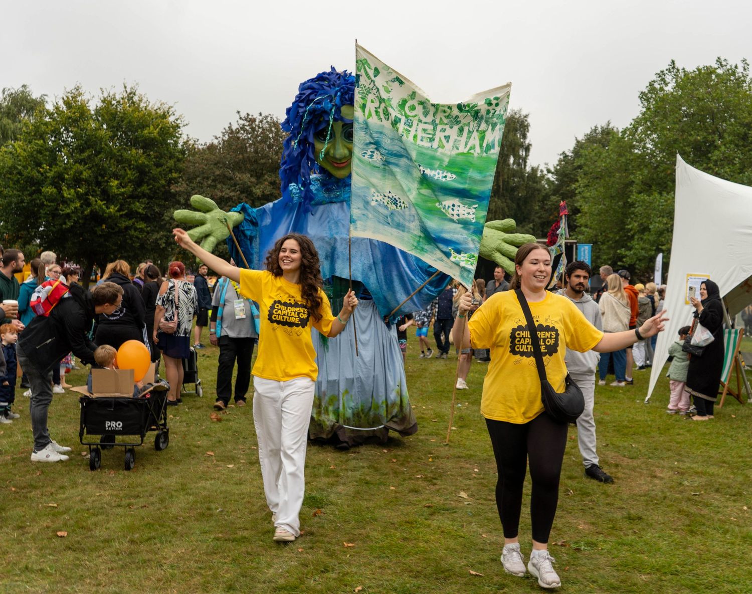 People carrying colorful fabric banners at outdoor festival event.
