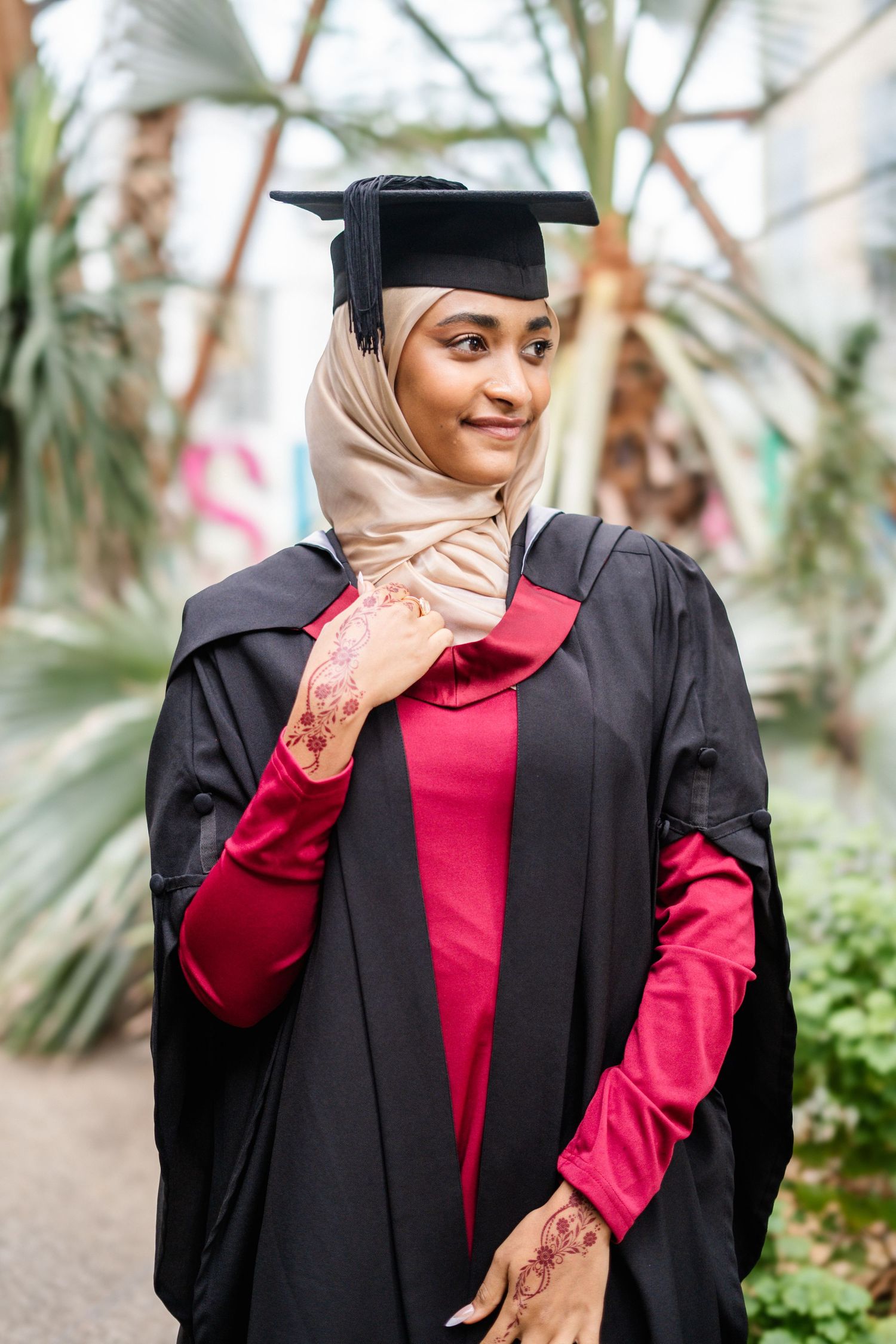 Candid graduation portrait with palm trees and greenhouse setting.