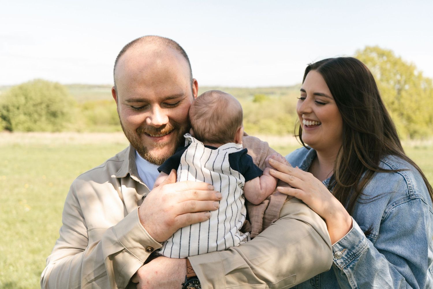 Family enjoying a tender moment together on a blanket outdoors in a sunny field.