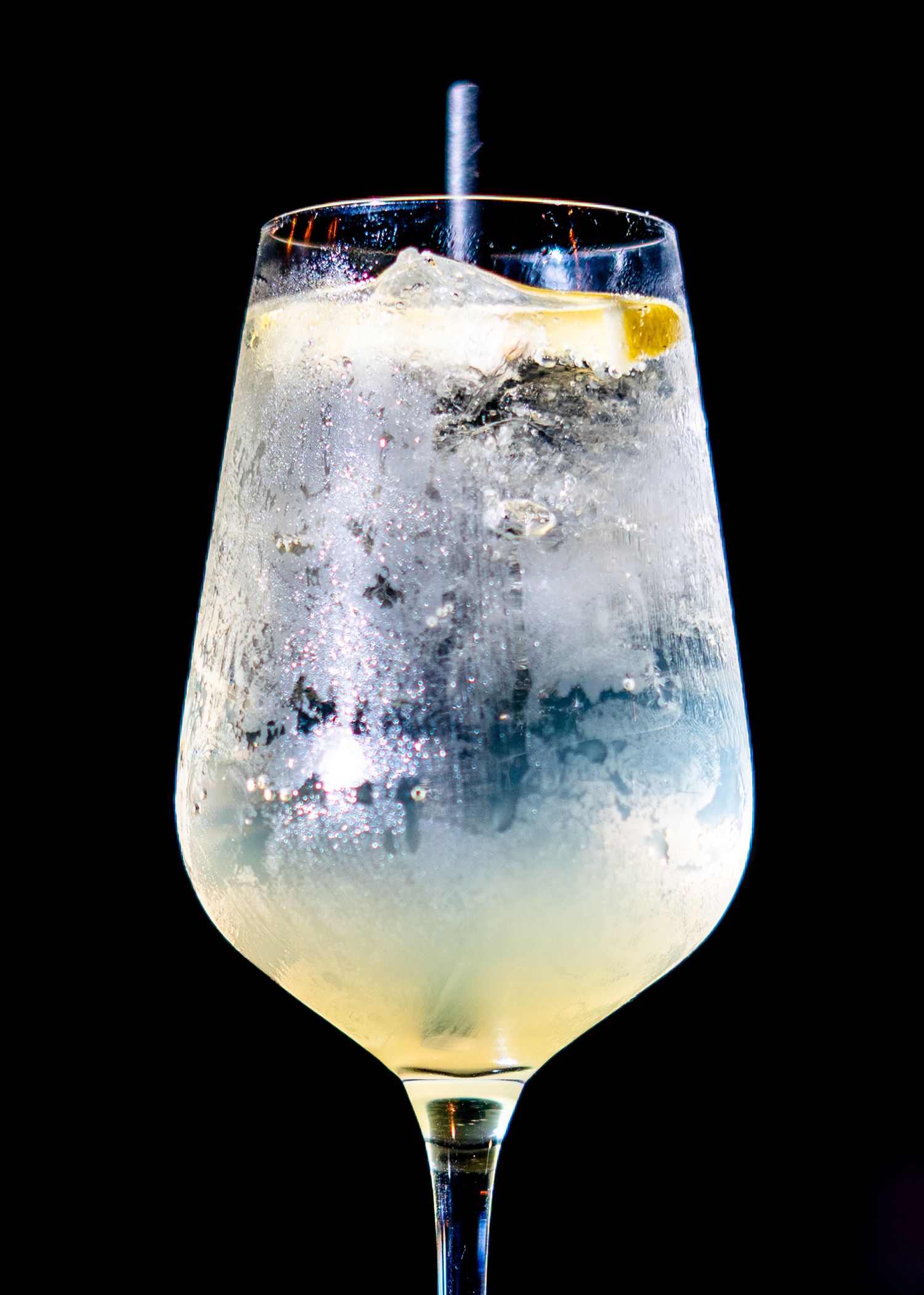 Frosted cocktail glass filled with clear liquid and ice against black background.