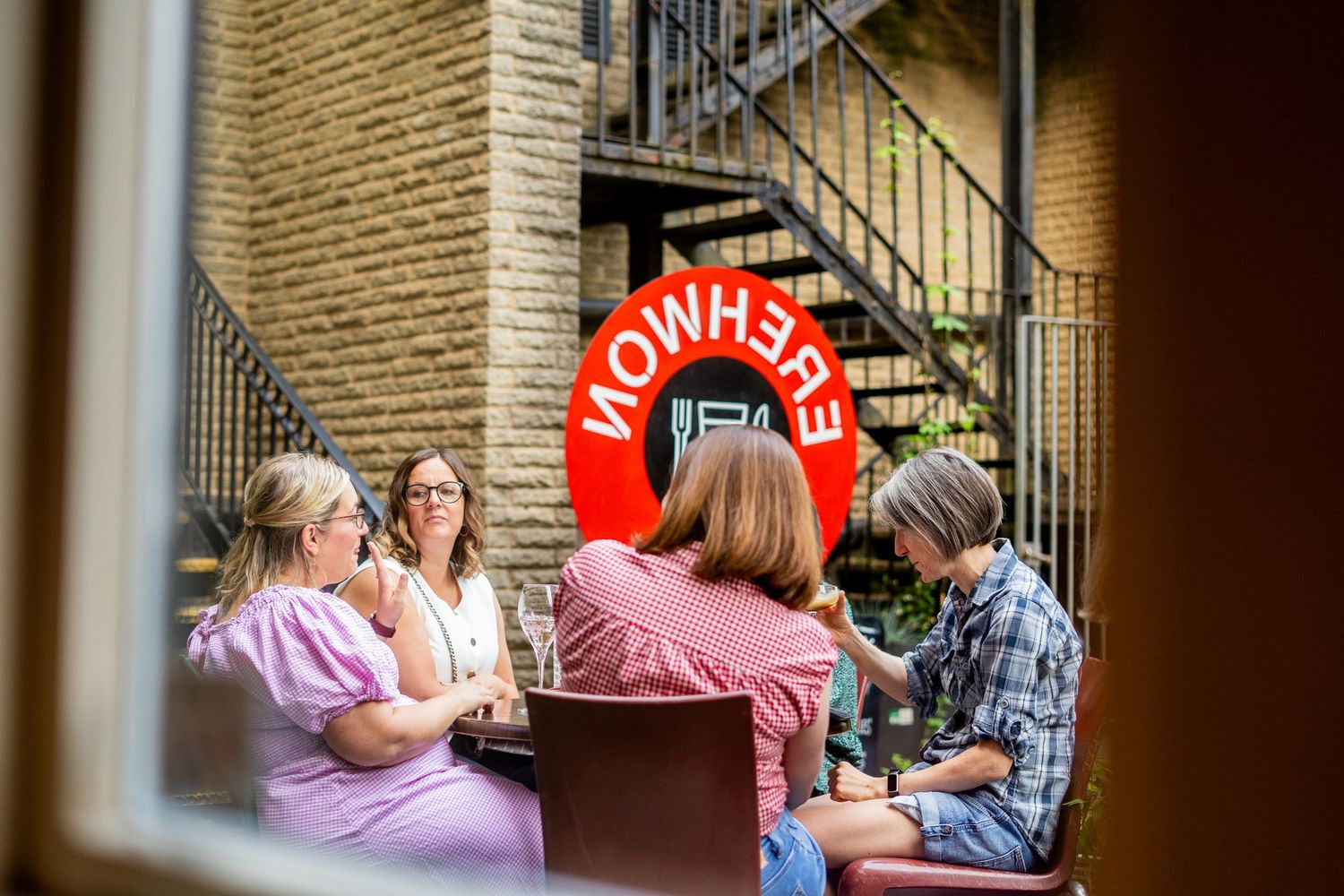 People enjoying drinks and conversation at an outdoor patio seating area with brick walls.