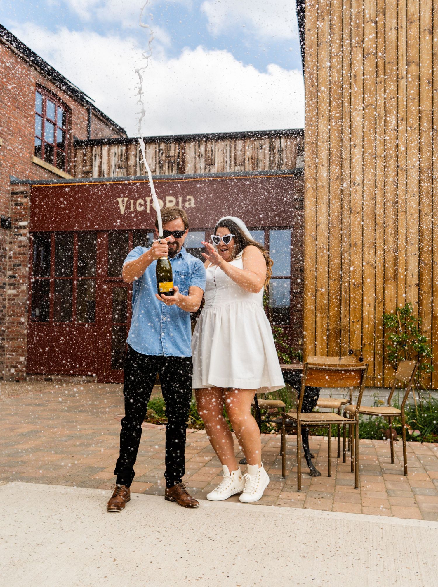 Celebration sequence with champagne outside Victoria venue featuring wooden and brick architecture.