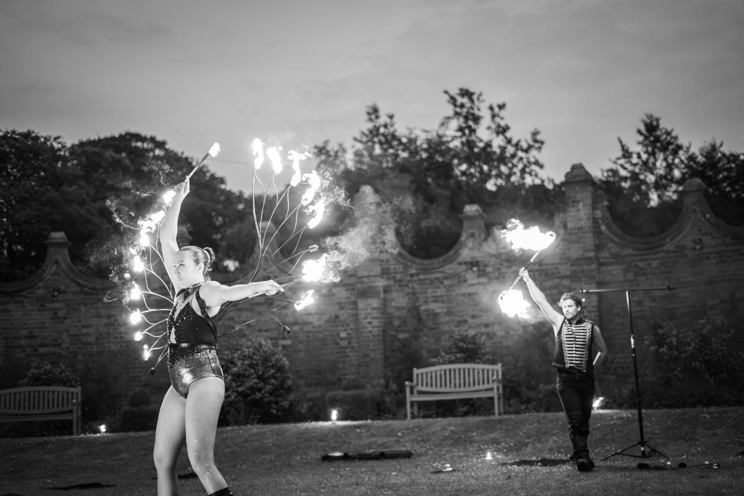 Dramatic black and white photo of fire performers spinning flames in an outdoor venue.