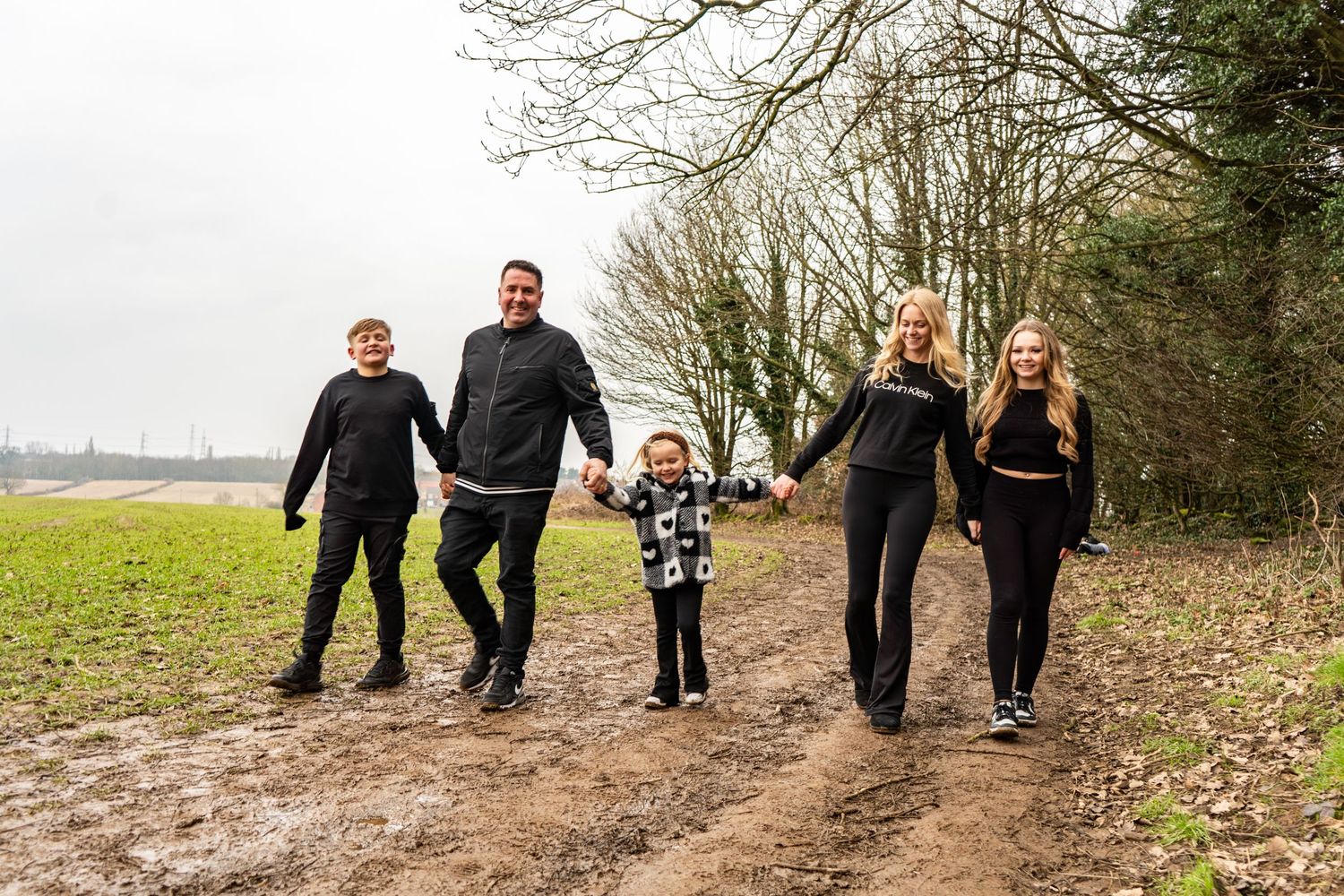 A family walking together on a dirt path through a wooded area.