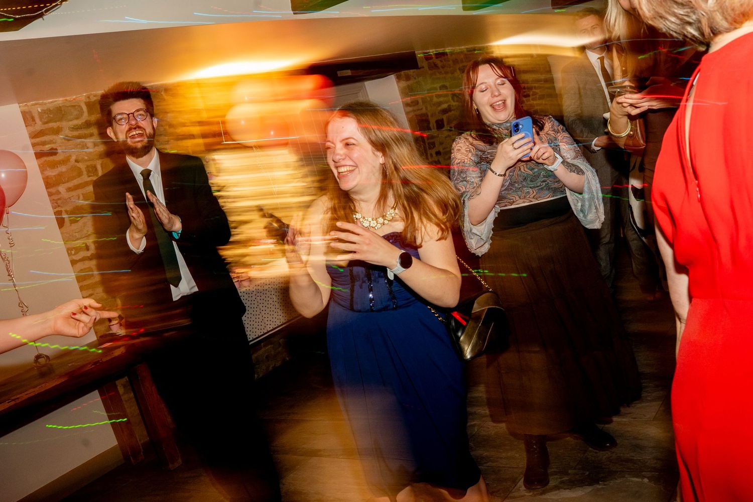 Energetic dance floor moments captured at an indoor celebration with brick wall background.