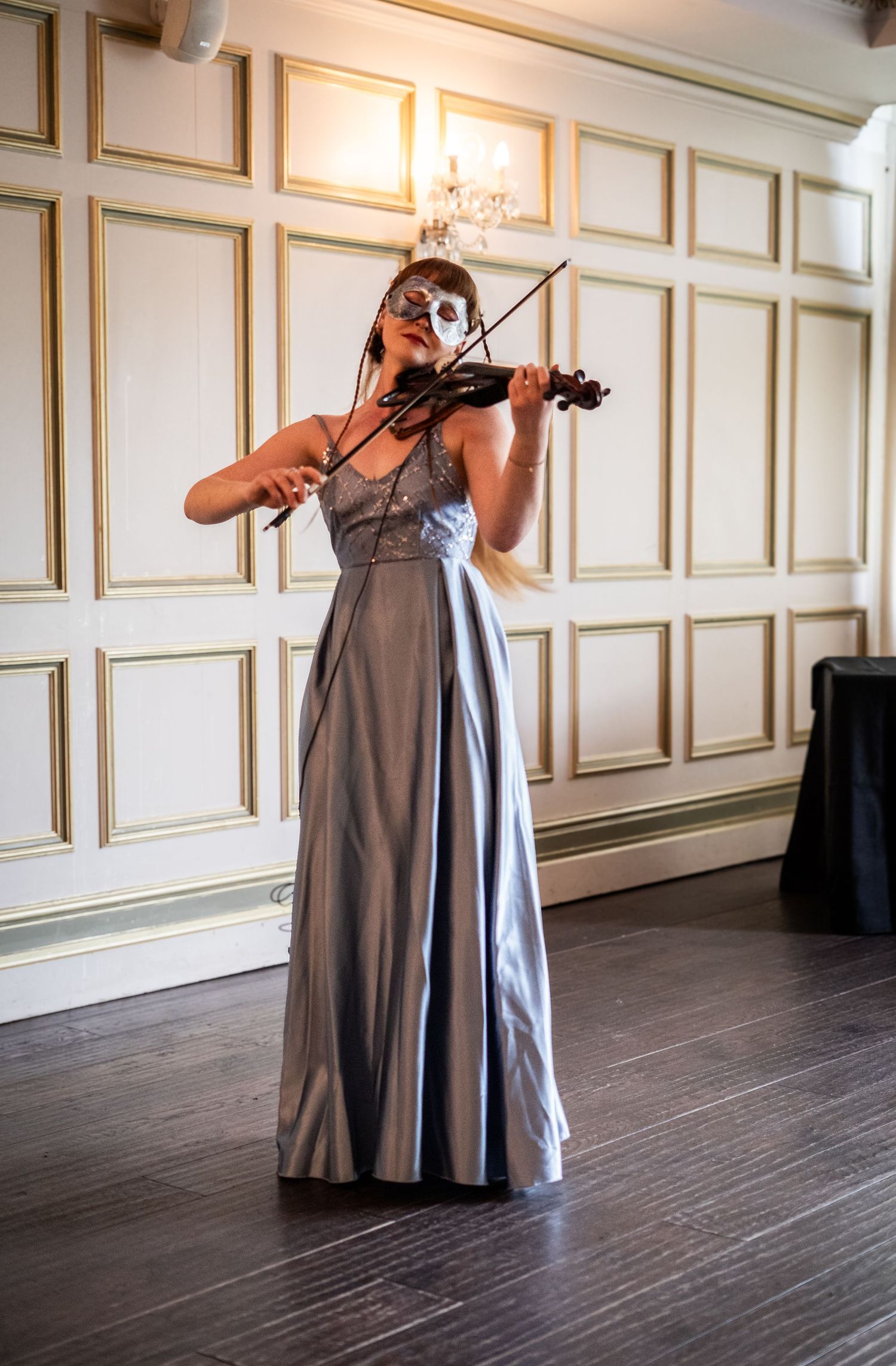 Musicians performing with violins in an elegant room with white paneled walls and wooden floors.