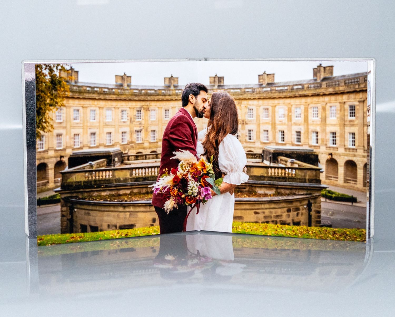 A romantic couple shares a tender moment in front of a grand historic building with a bouquet of flowers.