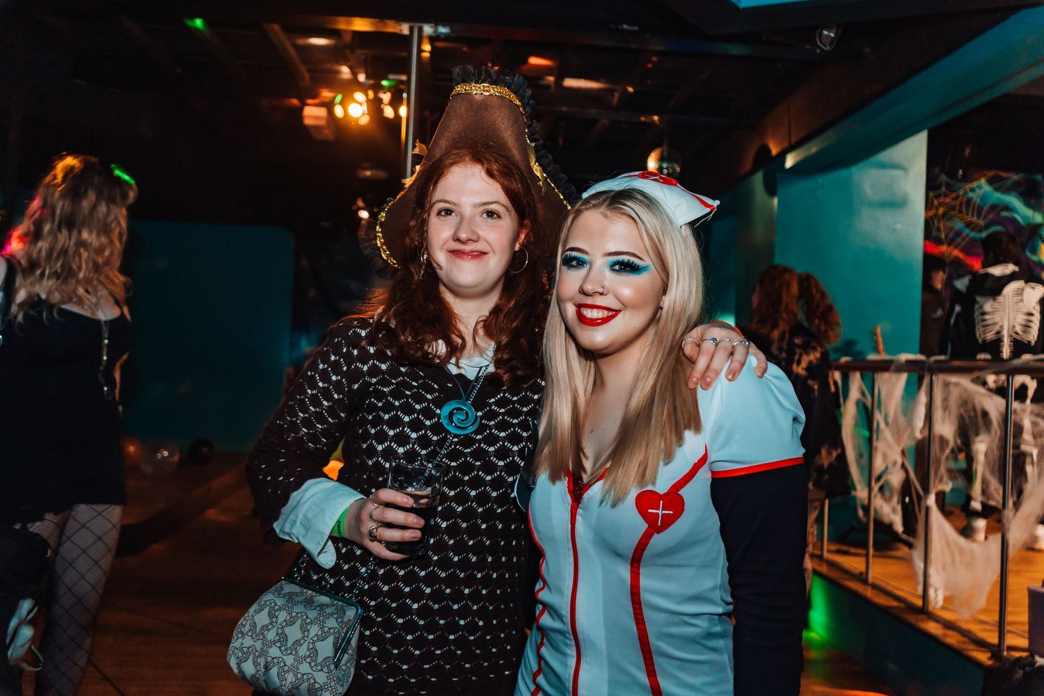Two party-goers enjoying a night out at a dimly lit club with colorful lighting.