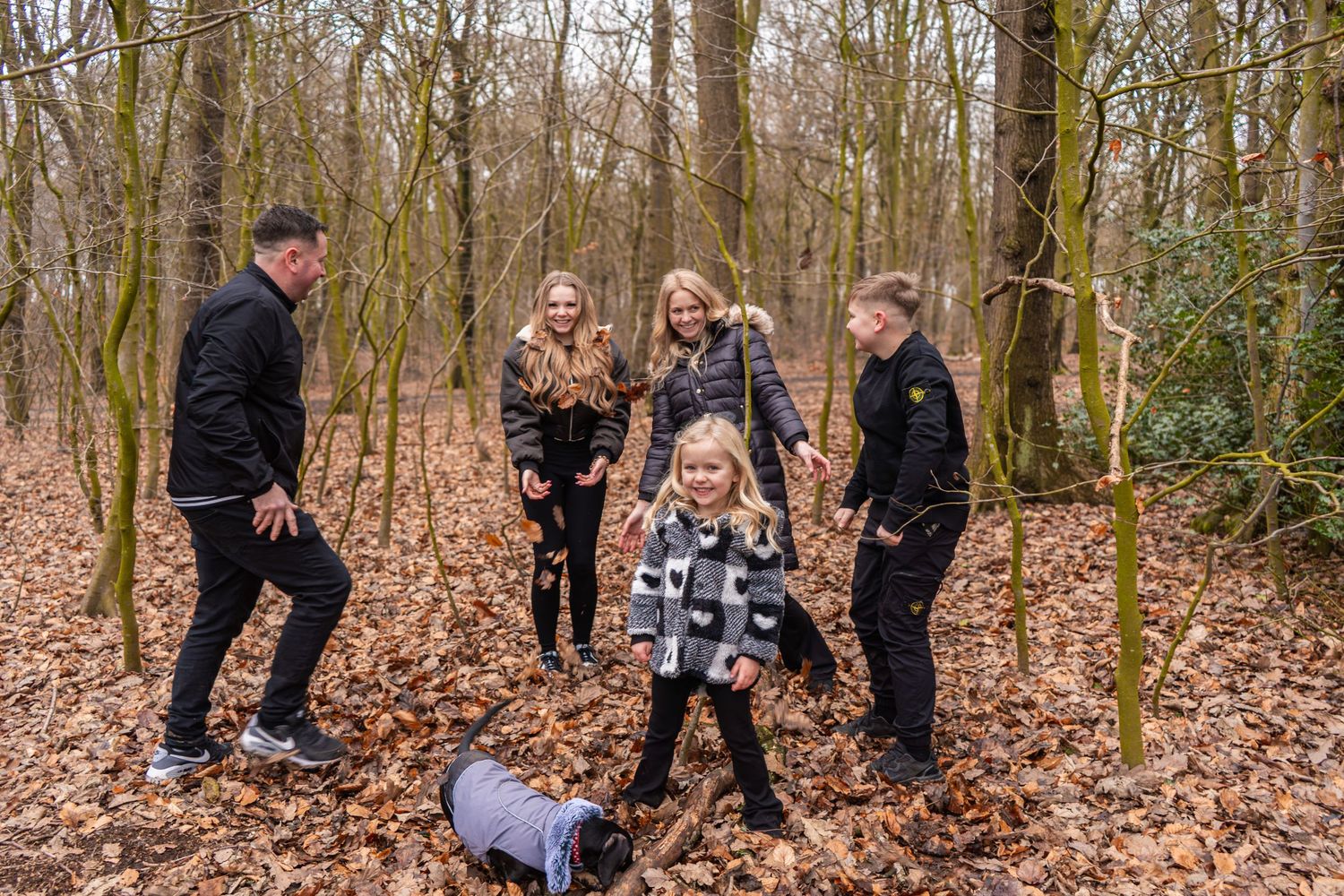 A group plays and dances together in a wooded area covered with fallen leaves.
