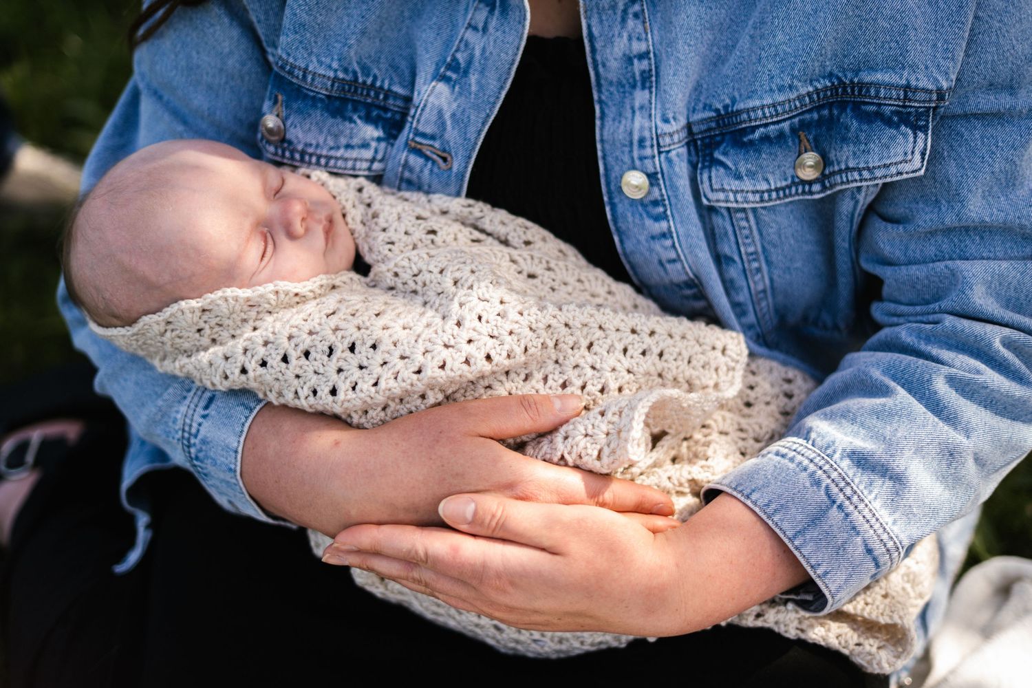 Newborn baby sleeping peacefully in crocheted wrap against denim backdrop.