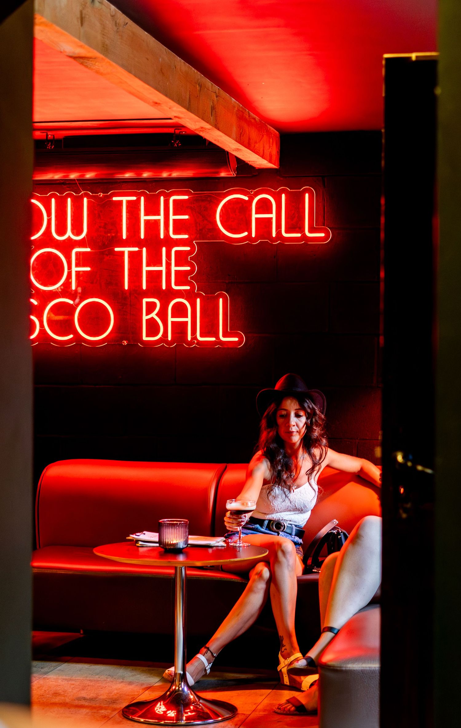 Red neon signs illuminate a modern bar interior with lounge seating.