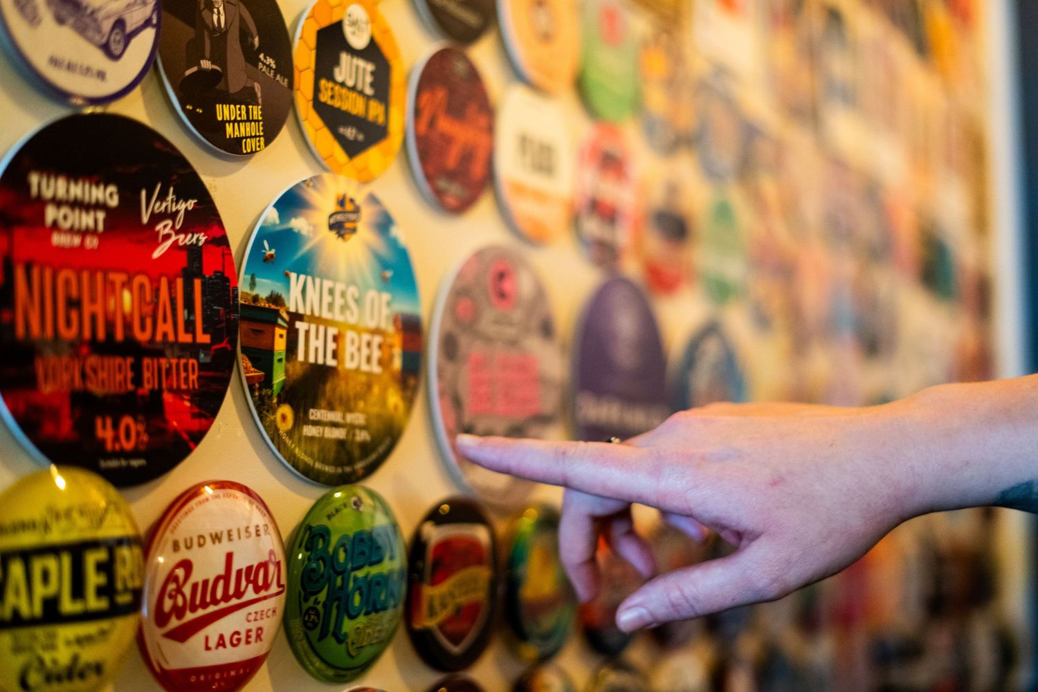 Collection of colorful beer tap handles and brewery stickers displayed on a wall.
