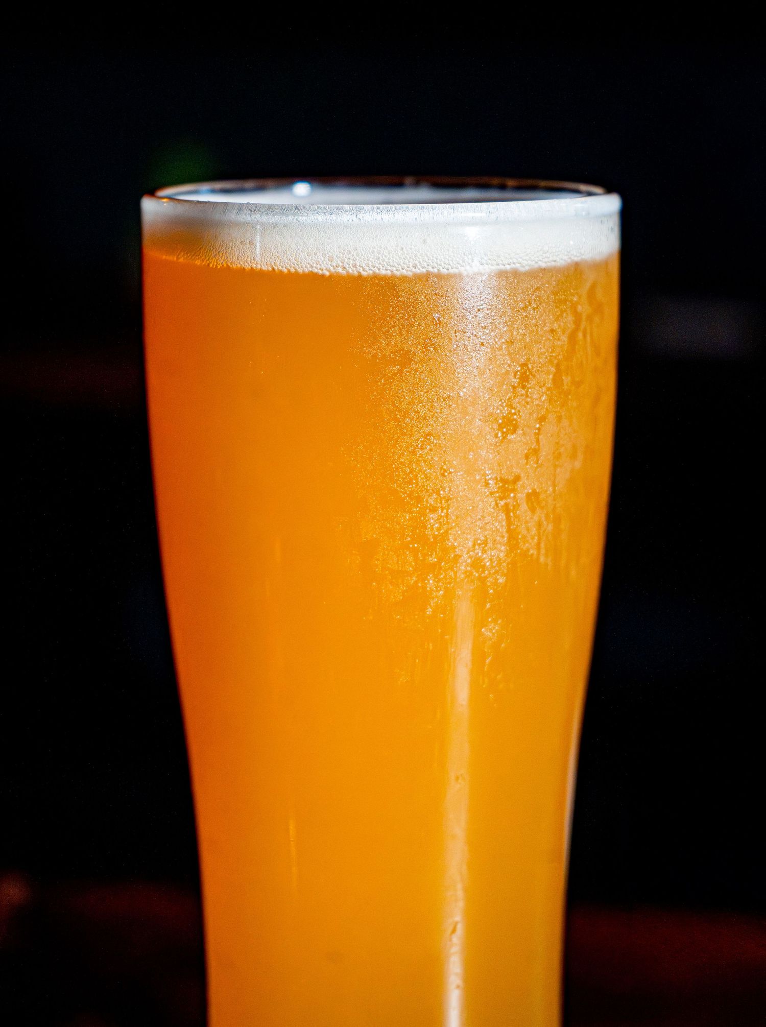 A tall glass of unfiltered craft beer with a foamy head and condensation on the glass.