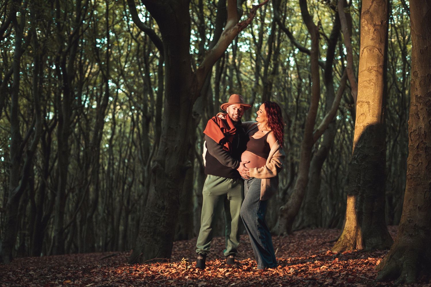 A couple walks through a scenic autumn forest path covered in fallen leaves.