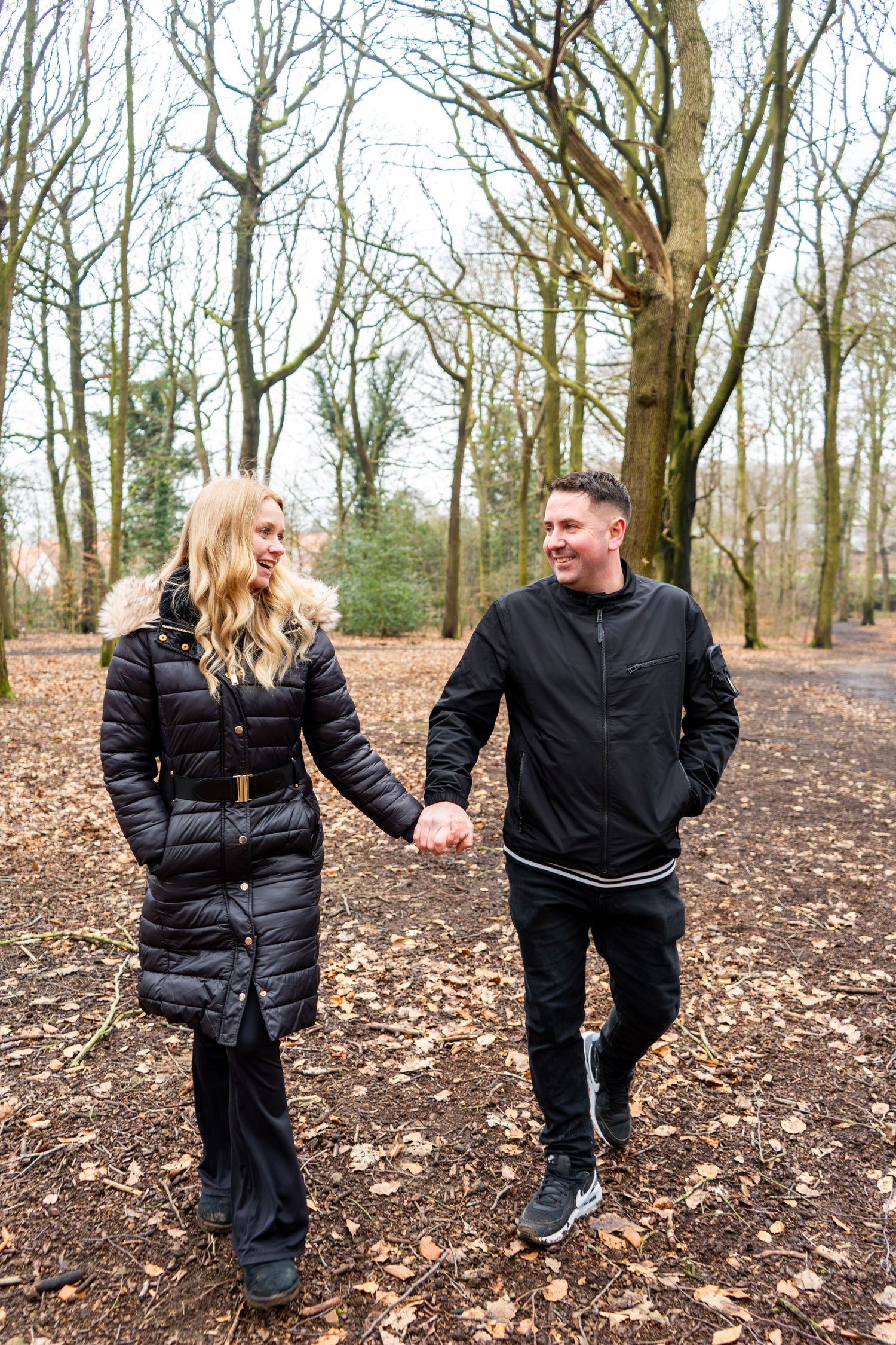 Two people in black jackets playfully interacting on a woodland trail.