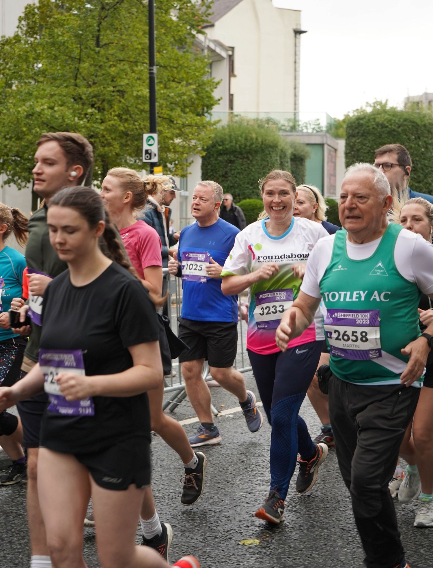 Athletes racing through a city street with race numbers visible on their shirts.