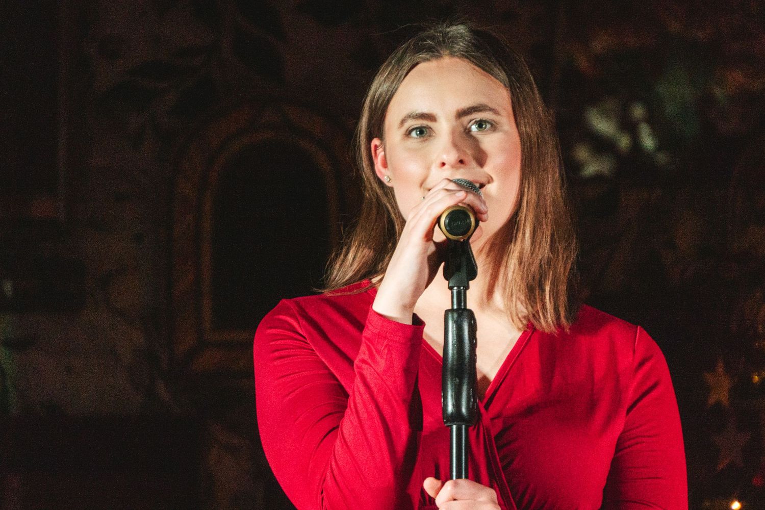 Singer performs with microphone on stage in red attire during evening concert.