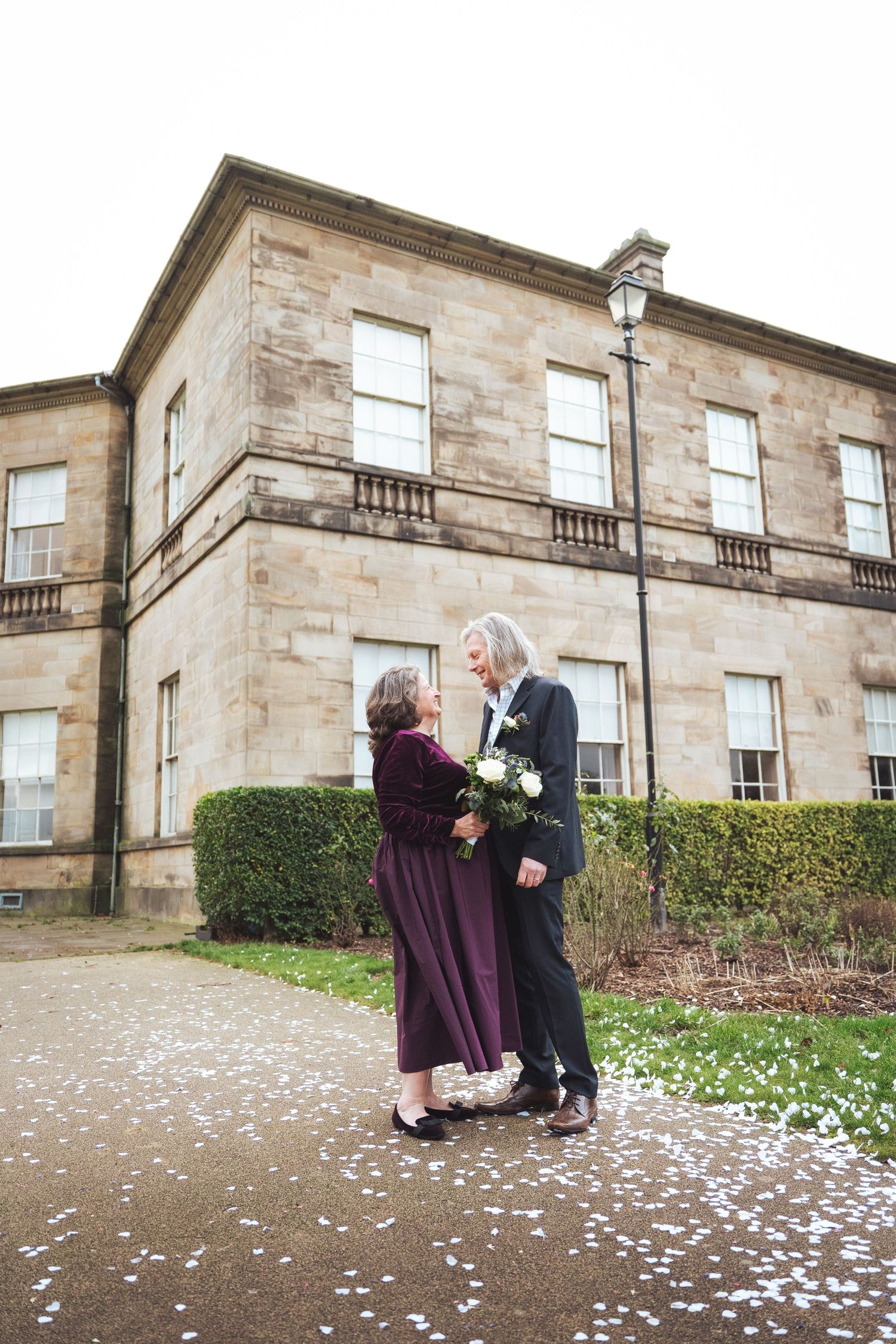 Wedding sequence with flower petals scattered on ground outside stone building.
