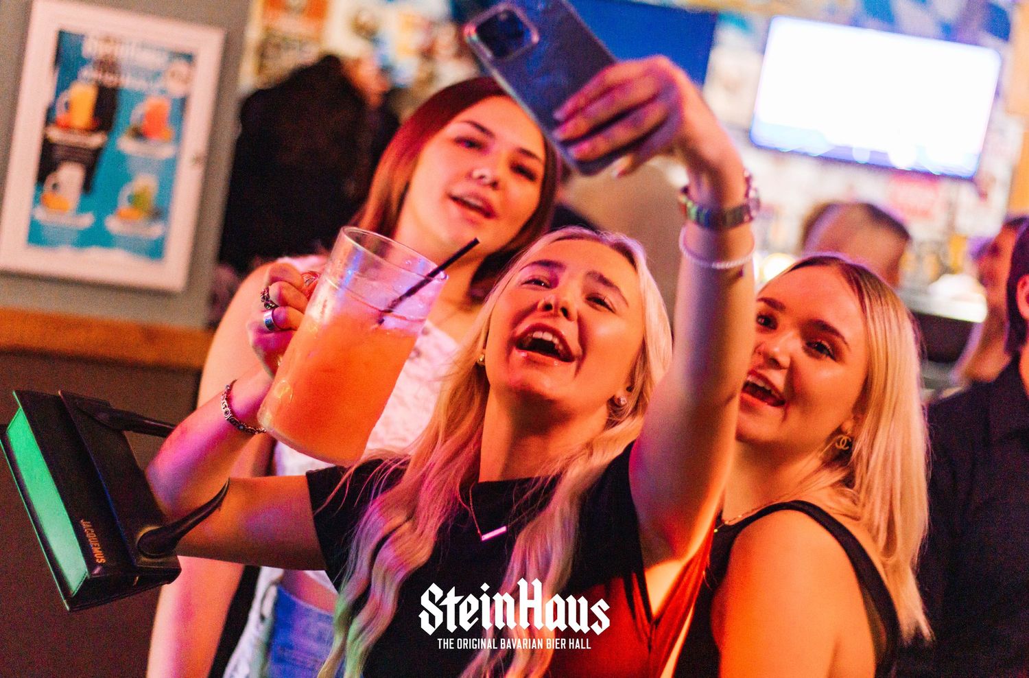 Enthusiastic patrons celebrating and laughing at Steinhaus nightclub under colorful lighting.