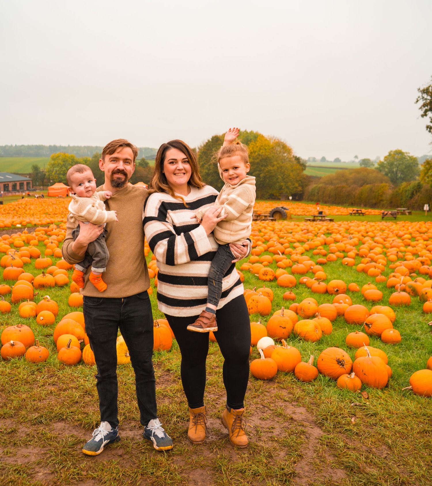 Family poses together in a pumpkin patch field during autumn.